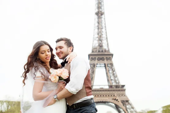 Couple de mariés avec un bouquet devant la tour Eiffel.