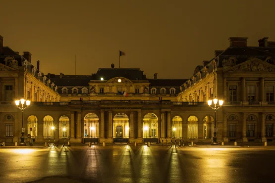 Façade du Palais-Royal illuminée la nuit, devant une cour pavée.